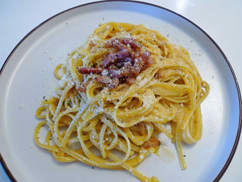 Plate of spaghetti carbonara topped with grated cheese and bacon on a white plate. Creamy and appetizing look with a simple background.