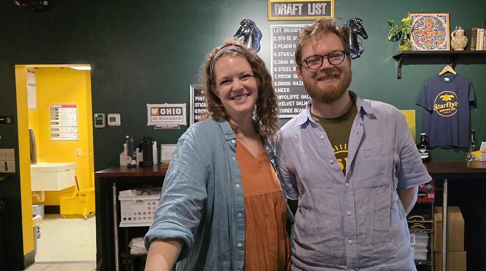 Owners Bailey Archer and Ethan Comfort smiling behind the bar inside their Canton taproom.