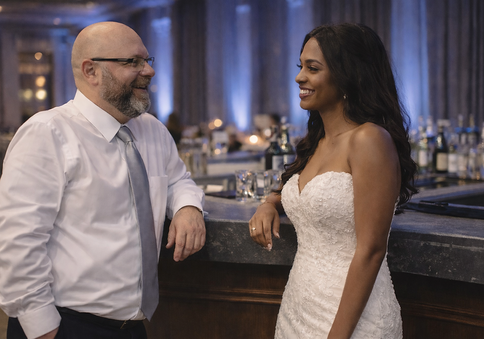 Wedding DJ Alan Mostov smiling while talking with a bride at a softly lit reception bar area.