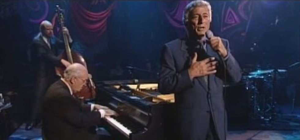 Tony Bennett performs on MTV Unplugged, singing into a handheld microphone while accompanied by a jazz trio featuring piano, upright bass, and drums on a softly lit stage.