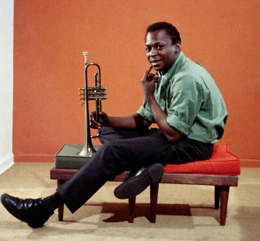 Jazz trumpeter Miles Davis seated with a trumpet during a studio portrait.