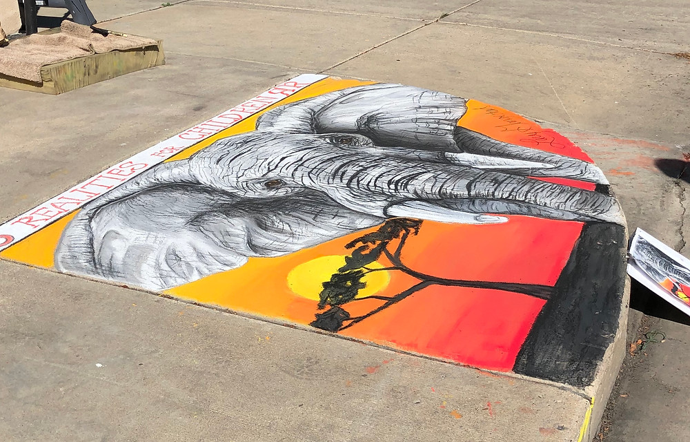 A sidewalk pastel painting of an elephant with a vibrant sunset background.