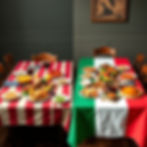 Two tables with American and Italian flag tablecloths, each set with dishes and red wine. A painting decorates the gray background wall.