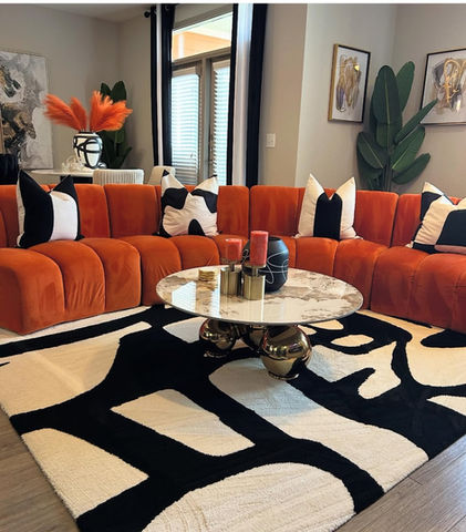 Bold modern living room with burnt orange curved sectional sofa, black-and-white rug, and vibrant decor accents.