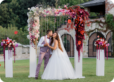 Bride and groom kissing at wedding arch, floral decor