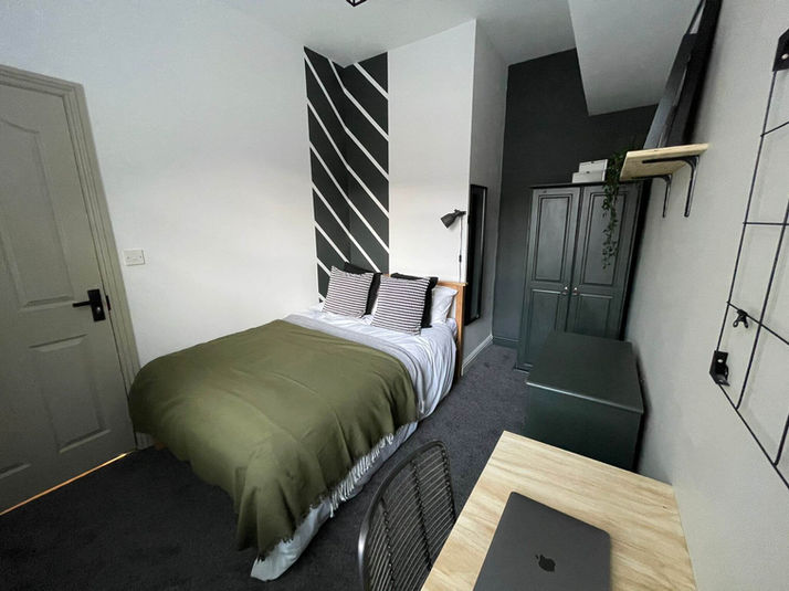 One of five bedrooms in this student property, this room has a double bed with green and white bedding, as well as a wooden desk complete with a modern metal desk chair.

The walls are dark grey and white for a modern and stylish finish.