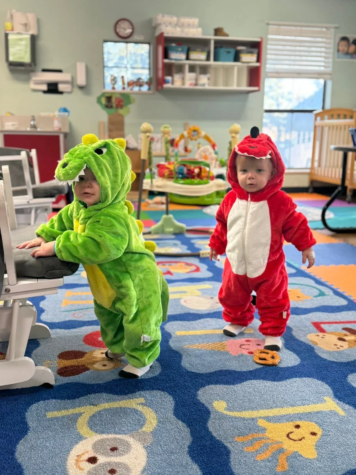Two young children in green and red dragon costumes in their classroom