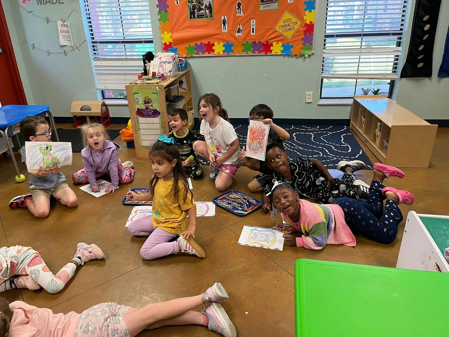 Children smiling, coloring, and showing their drawings together on the classroom floor
