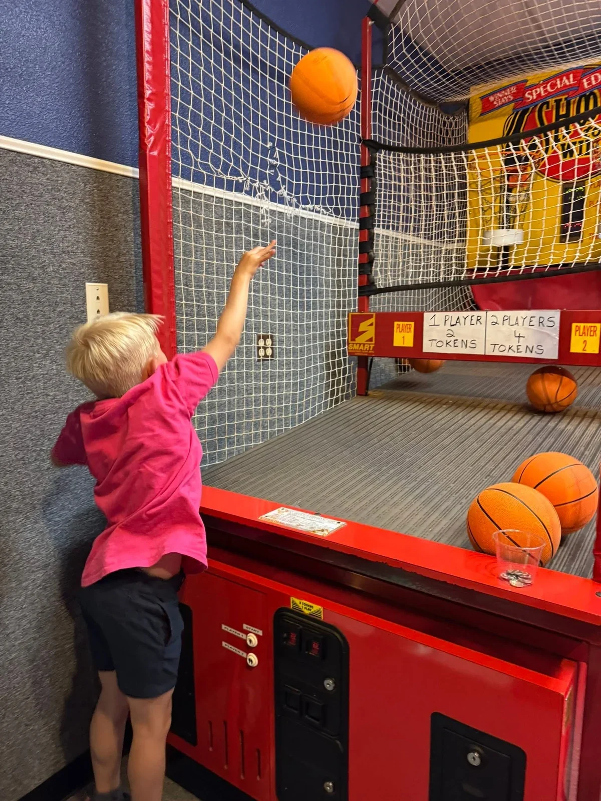 A child in a school shirt shooting a basketball at an arcade on a field trip