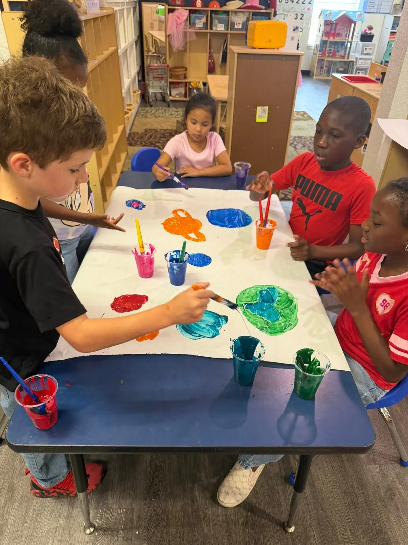 Children painting a colorful picture together at a classroom table