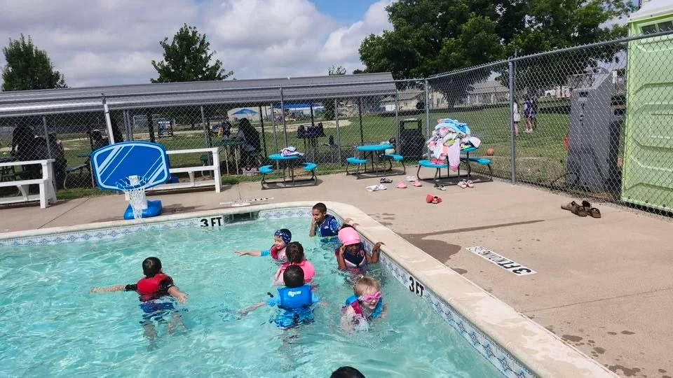 Children playing together in the school pool with the poolside basketball hoop and campus beyond