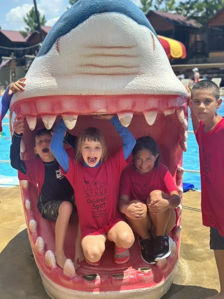 Children in Children’s Spot shirts posing inside a giant shark sculpture at Pirates Cove