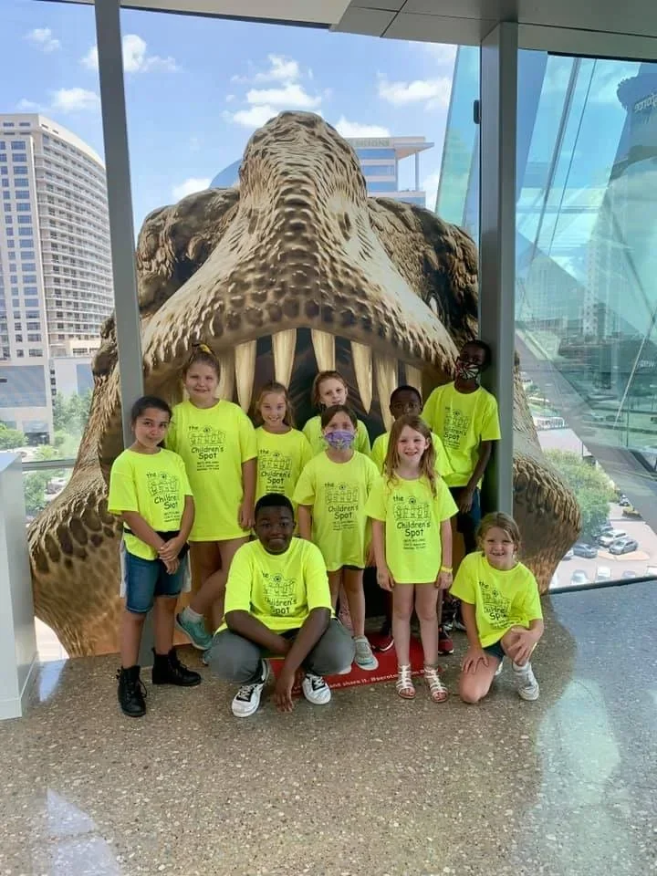 Children in matching school shirts on a museum field trip beneath a dinosaur exhibit