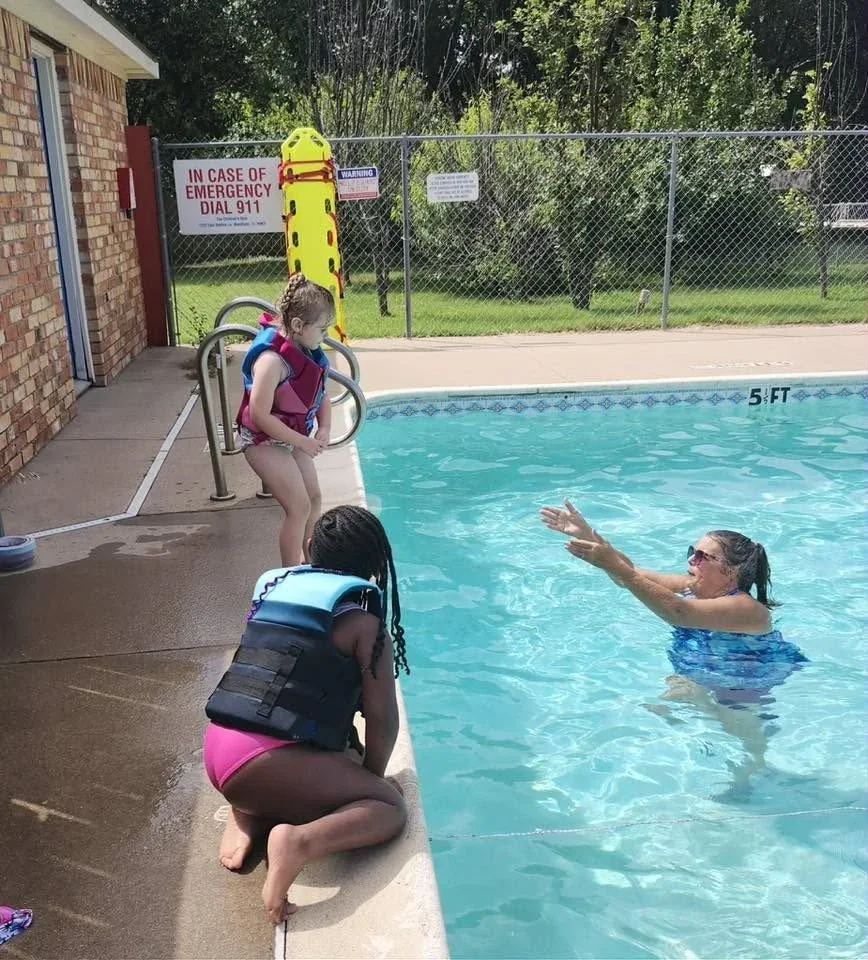 Children with adults at the edge of the school pool during Kinder-Prep Pool Day in June 2026