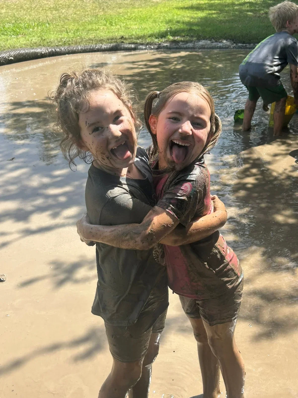 Two smiling friends sharing a muddy hug in The Children’s Spot mud pit