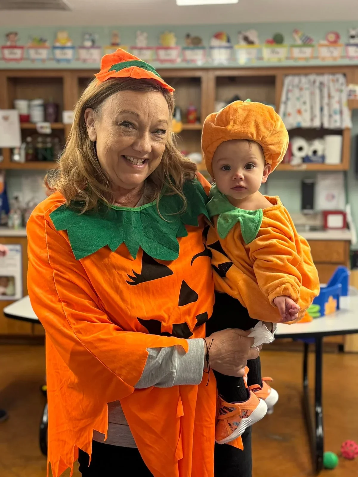 A smiling school adult holding a child, both dressed in pumpkin costumes for Boo Fest