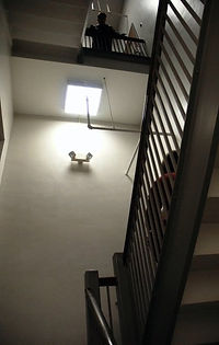 A woman sits in a stairwell with a dark figure looking at her from above