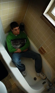 A man lays clothed in a bathtub clutching a framed photo
