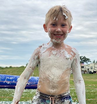 A smiling child covered in shaving cream after completing Kiesler’s Campground backyard obstacle course.