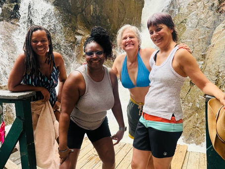 Four women stand next to a waterfall.