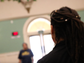 A person with locks has there back to the camera an dis facing two blurry out dancers.