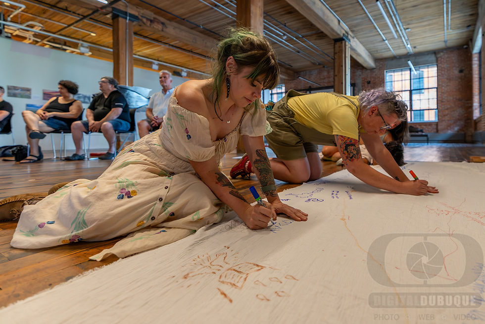 Audience members sit on the floor and draw and write on a large pice of white cloth.