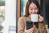 Portrait image of a woman holding and using mobile phone while drinking coffee in cafe_edi