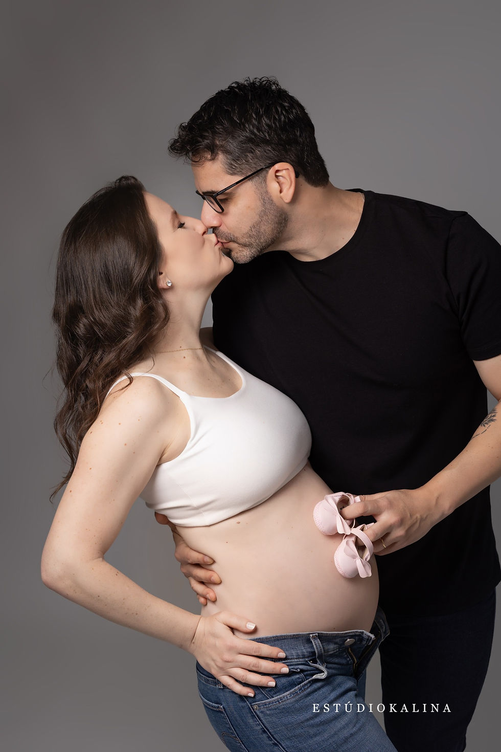 Casal se beijando com sapatinhos de bebê durante o ensaio gestante