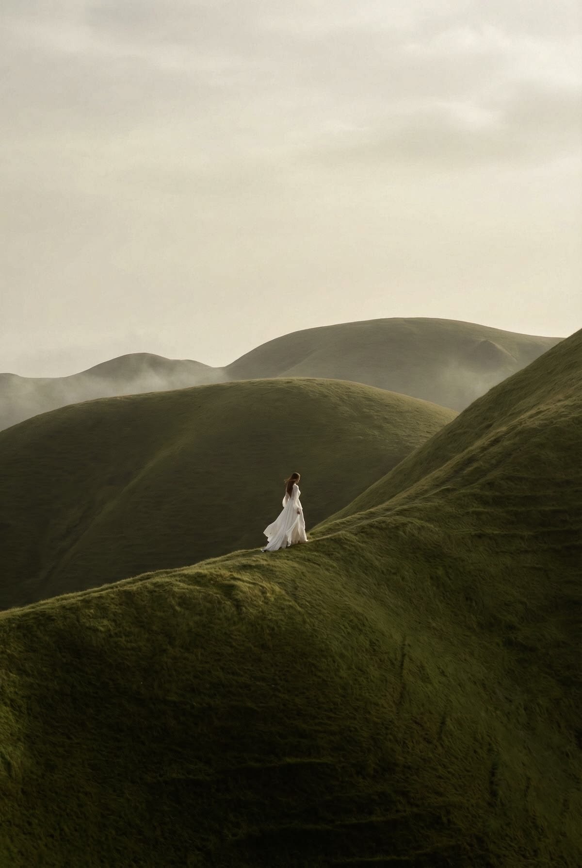 A woman in white on a path between gentle green hills.