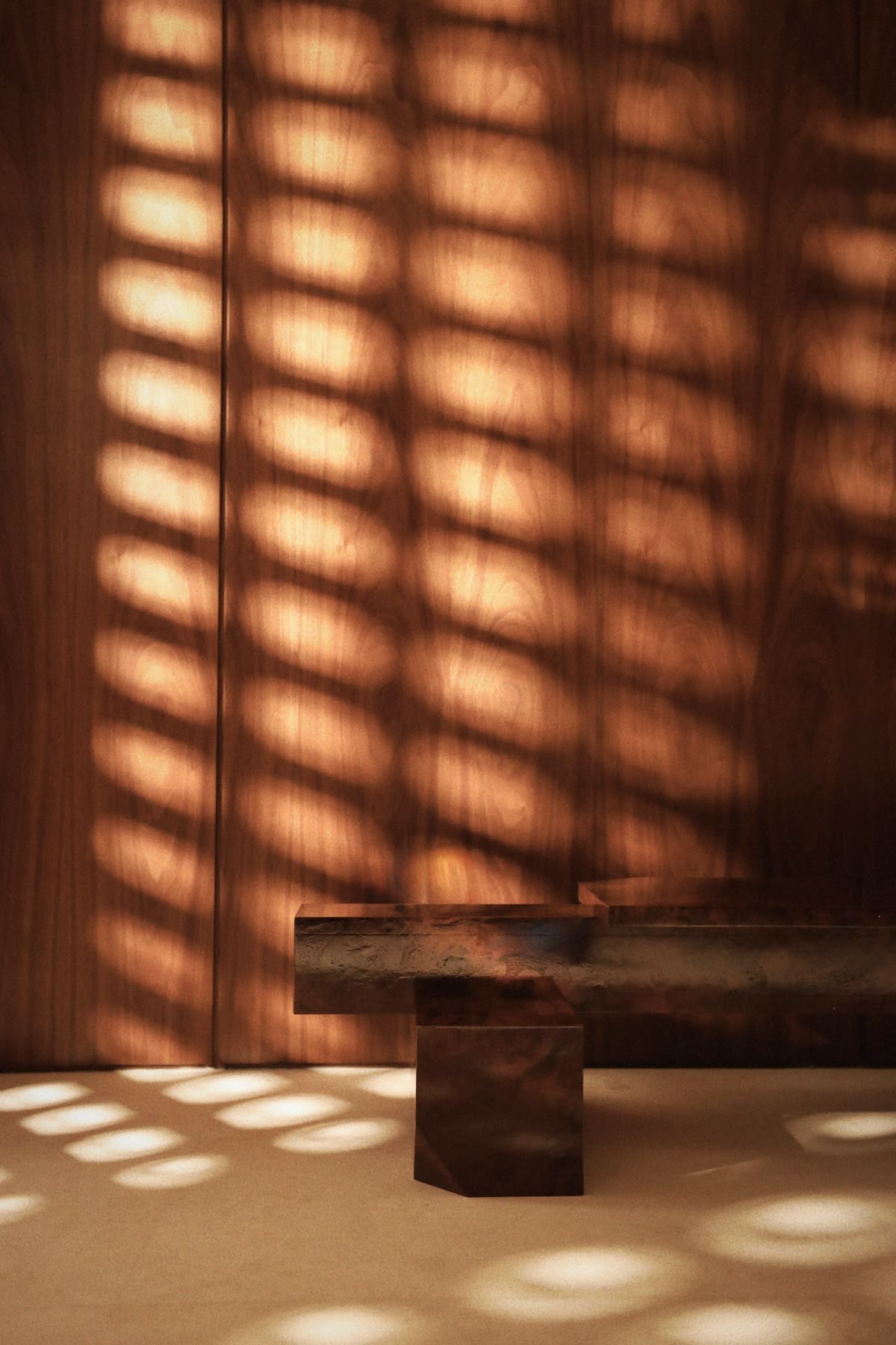 Sonnenlicht fällt durch ein Fenster und zeichnet weiche Schatten auf eine warme Holzwand und eine Bank.