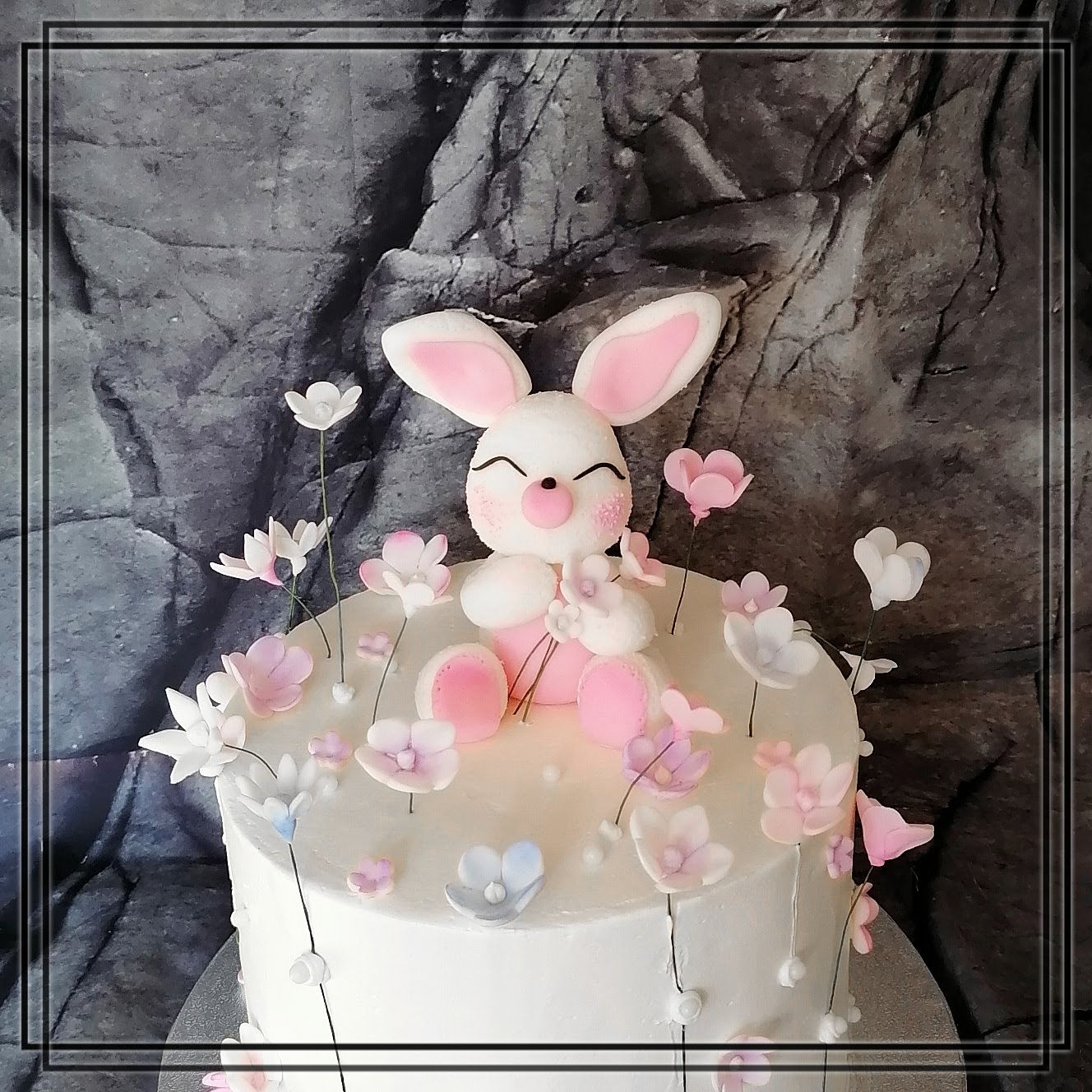 Handgefertigte Fondantfigur – süßes Häschen mit Zuckerblumen in Rosa, Weiß und Flieder auf einer Geburtstagstorte.