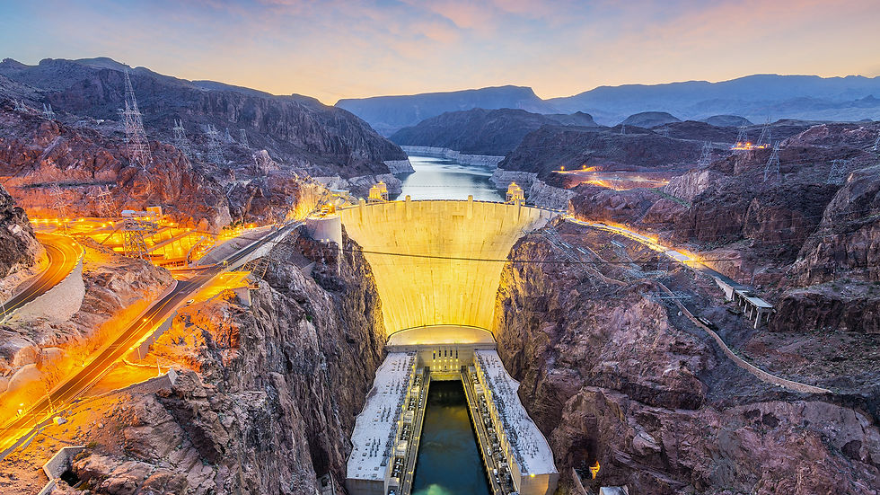 Illuminated Hoover dam at dusk with glowing orange roads and power lines. Surrounding rocky terrain and distant mountains under a colorful sky.