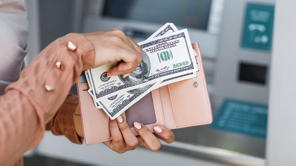 Hands hold $100 bills near a pink wallet in front of an ATM. Person wears a peach shirt with shiny buttons. The scene feels transactional.