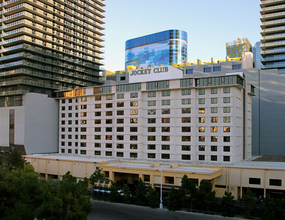 High-rise urban setting featuring the Jockey Club, a beige building with rows of windows. Modern towers and a blue glass structure in the background.