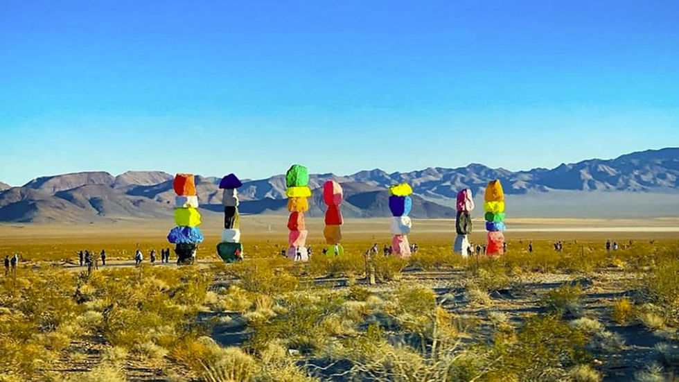 Colorful rock towers stand in a desert landscape with mountains in the background. People are walking around, enjoying the sunny day.