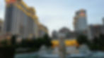 Statue in front of fountains at Caesar's Palace, Las Vegas. Tall buildings with illuminated signs and trees in the background, dusk sky.