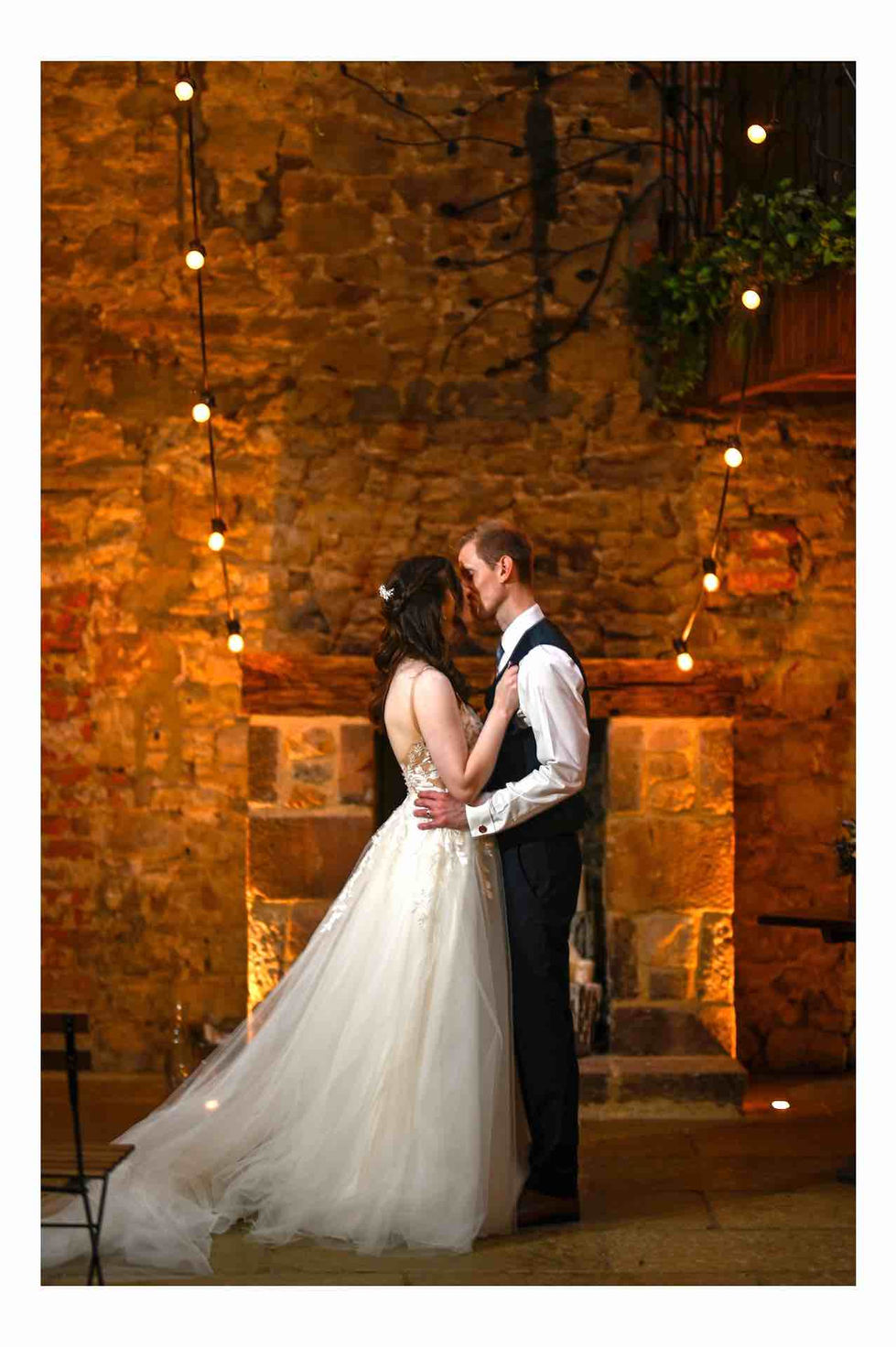 a bride and groom are kissing in front of a stone fireplace . at Doxford Barns