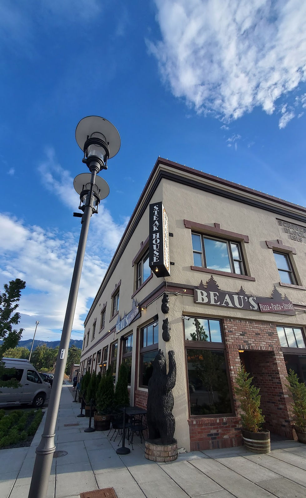 The exterior of the two-story Beau's Pizza and Pasta restaurant in Cle Elum on a clear day, with a distinctive black bear statue near the entrance.