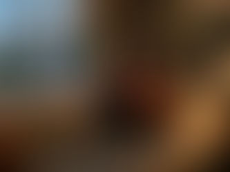 Woman sitting alone on a couch in a softly lit living room, looking out the window with a phone placed beside her, expressing loneliness and emotional withdrawal.