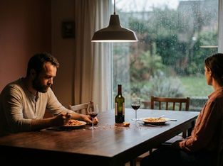 Man and woman sitting quietly at a dining table with wine, avoiding eye contact during a tense relationship moment