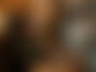 Woman sitting at a café table near a rainy window at night, holding a pen and looking outside with a thoughtful expression.