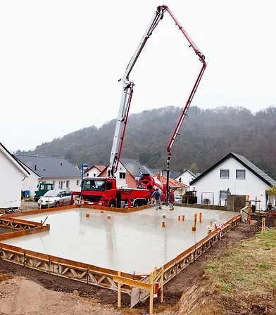 Crane working on poured foundation for house.