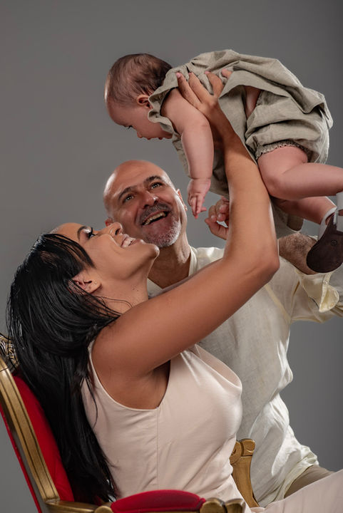 Pais felizes brincando com seu bebê, ambos olhando para cima com sorrisos enquanto levantam a criança no ar, transmitindo amor e conexão em um fundo neutro