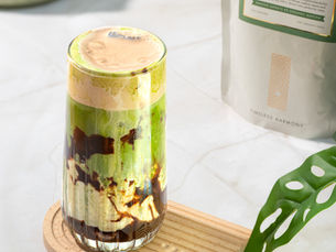 Layered Matcha drink with cream and chocolate drizzle in a clear glass
