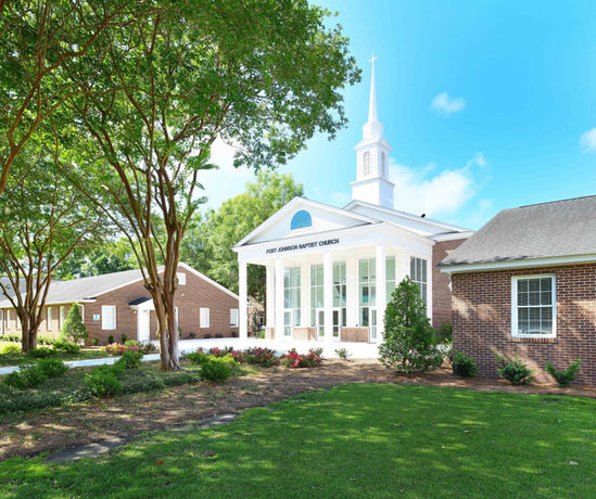 Exterior shot of First Baptist Church building with green lawn and trees.