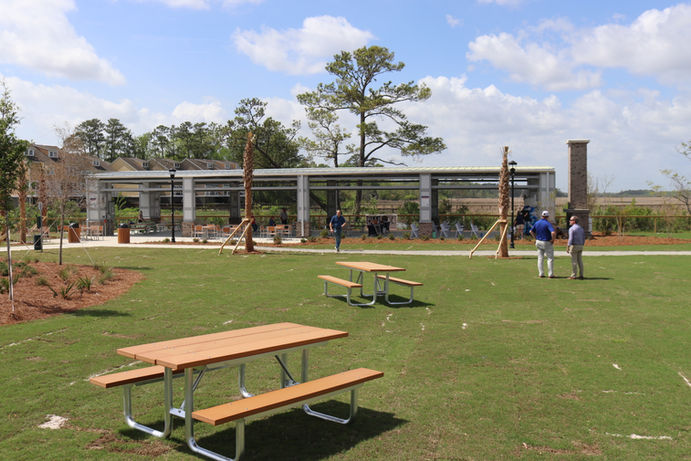 Picnic tables on green grass with a pavilion community design in the distance, sunny day at Steward Street Park in Hanahan