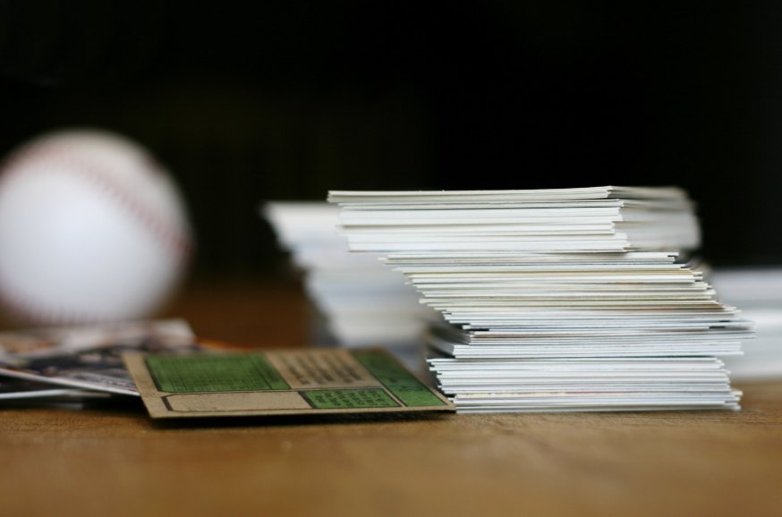 A stack of baseball cards on a wooden table next to a baseball