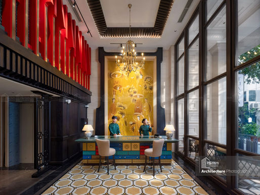 Ảnh chụp không gian lễ tân khách sạn phong cách Indochine với tranh nghệ thuật lớn, đèn chùm trung tâm và cửa kính cao đón ánh sáng tự nhiên.