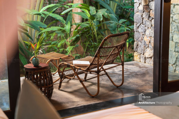 Góc thư giãn ngoài trời của villa resort với ghế mây và bàn trà nhỏ, nằm giữa không gian cây xanh và tường đá tự nhiên