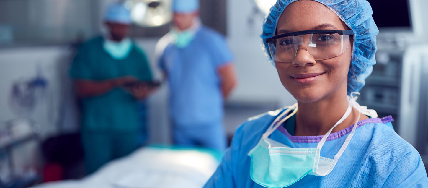 Portrait Of Female Surgeon Wearing Scrubs And Protective Glasses In Hospital Operating The
